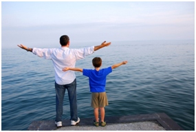 father and son standing on rock with arms wide overlooking the ocean